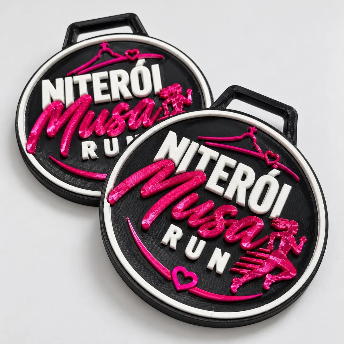 Duas medalhas pretas da corrida Niterói Musa Run com letras em rosa e branco em relevo